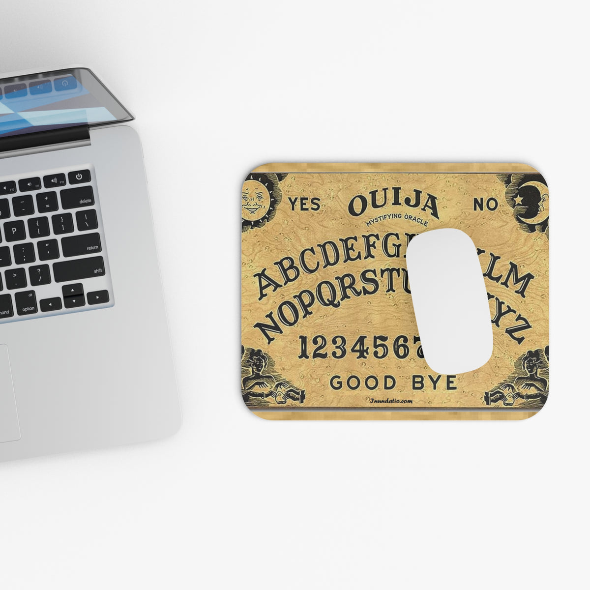 Ouija board mouse pad next to a laptop on a white surface
