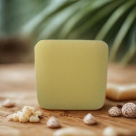 Green bar of soap on a wooden surface with blurred green leaves in the background