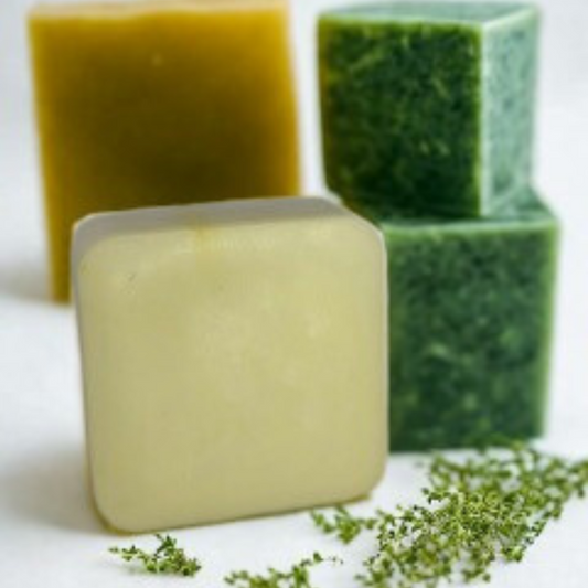 Three bars of soap in different colors on a white surface with greenery.