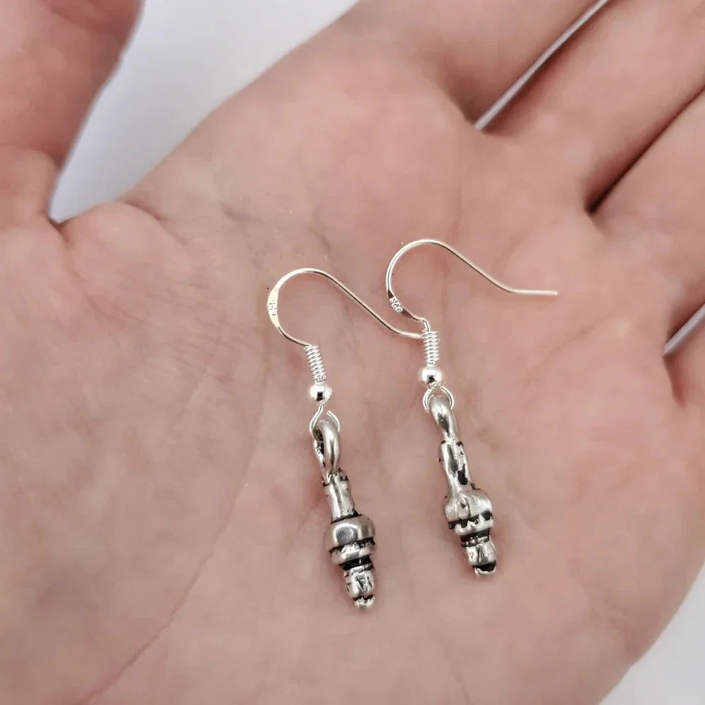 Silver earrings held in a hand against a neutral background