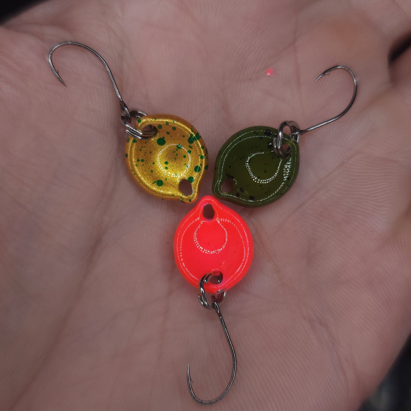 Three colorful fishing lures on a person's palm