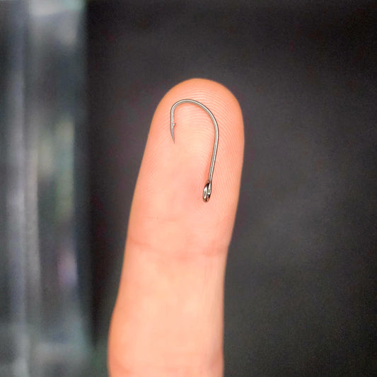Small fishing hook on a finger against a dark background