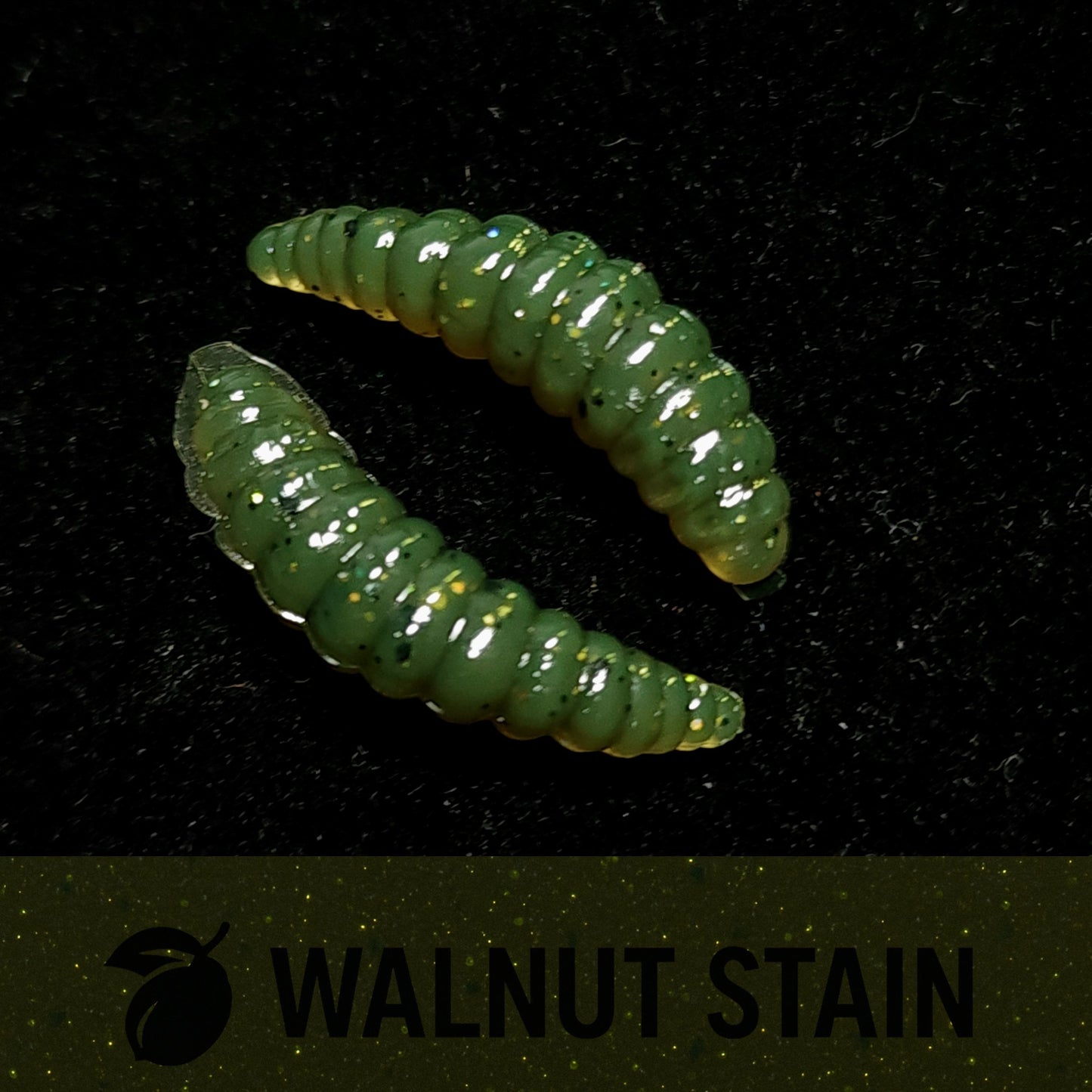 Two green larvae fishing lures on a black background with 'Walnut Stain' branding.