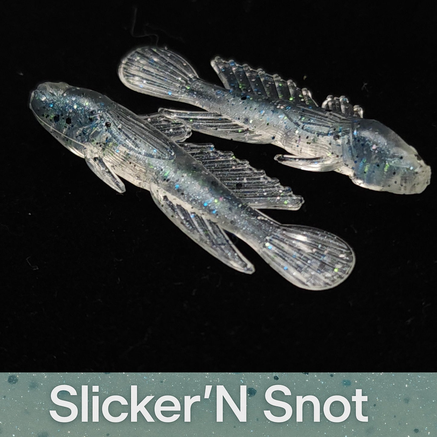 Two transparent fish-shaped lures with glitter on a black background, branded 'Slicker'N Snot'.