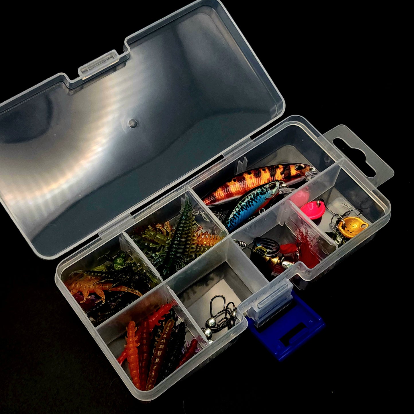 Open tackle box with various fishing lures on a black background