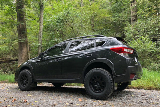 Black SUV with off-road tires and mud flaps parked on a gravel path surrounded by trees