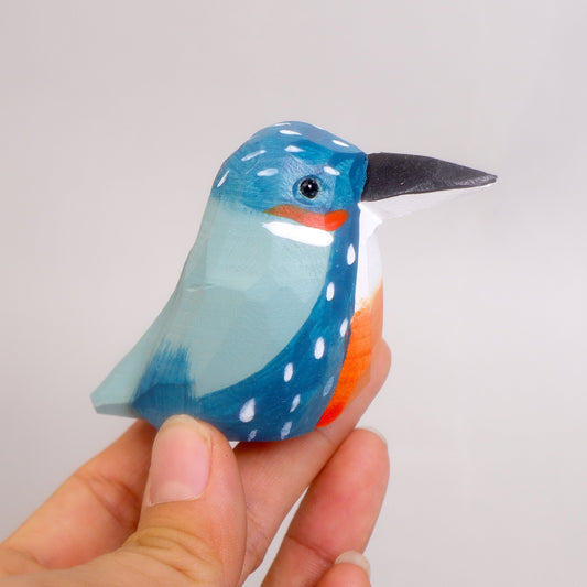 Hand holding a blue bird figurine with a white polka dot pattern on a light gray background