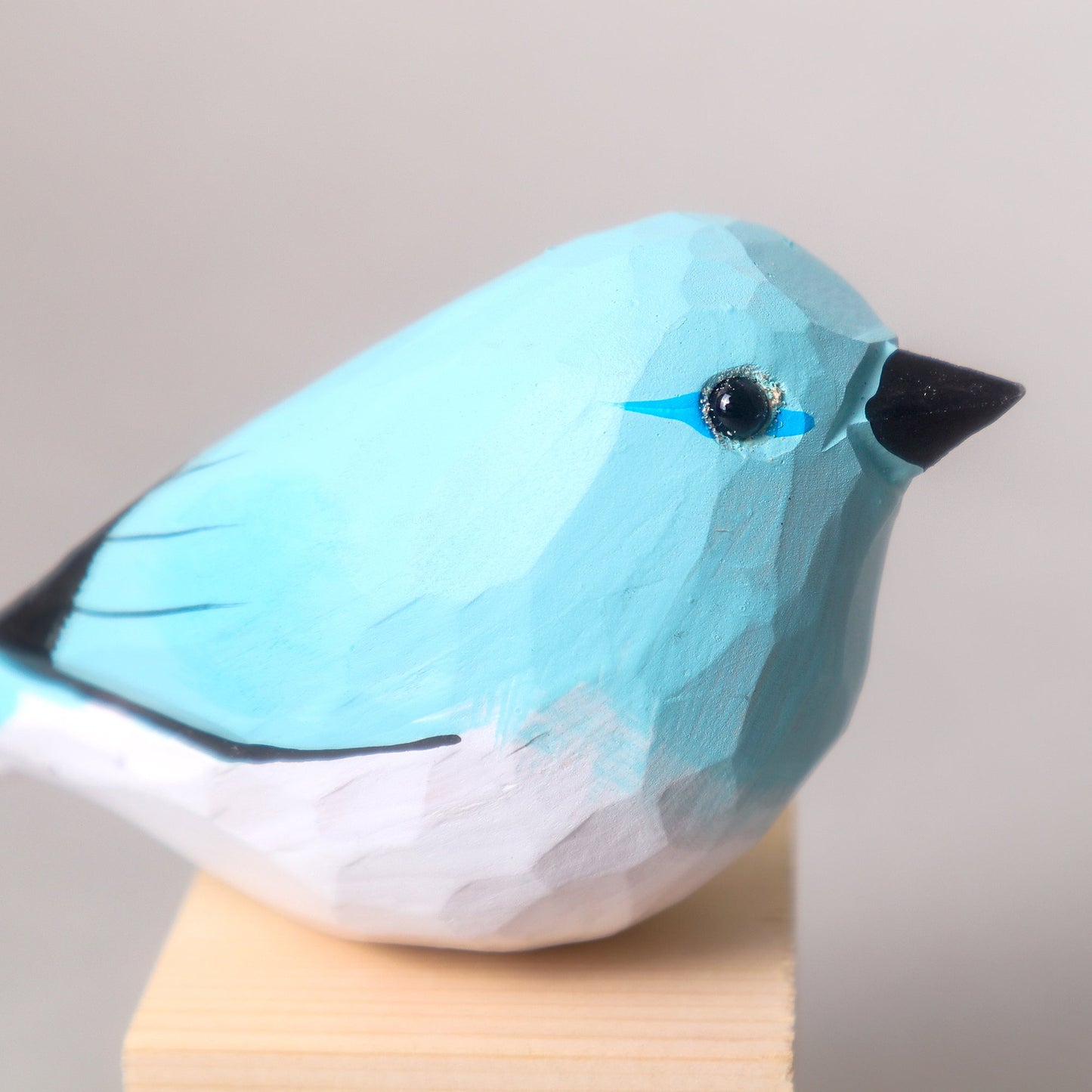 Blue bird figurine on a wooden stand with a plain background