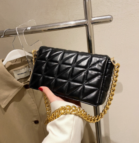 Black quilted handbag with gold chain held by a hand against a neutral background