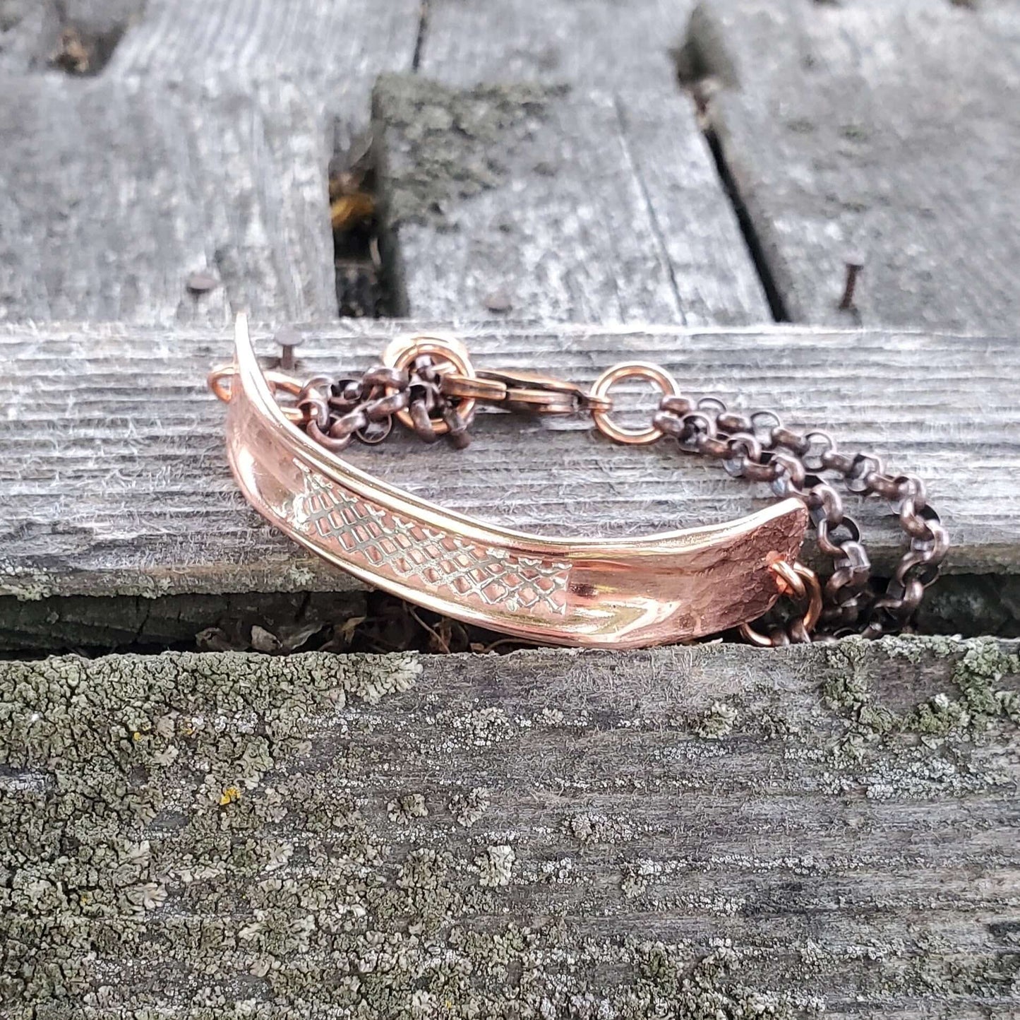 Crescent moon-shaped copper bracelet on a chain against a wooden background