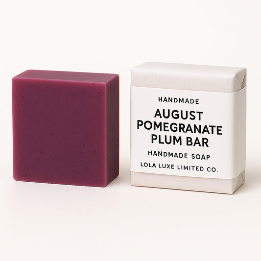 August Pomegranate Plum Bar. Purple handmade soap bar next to its packaging on a white background