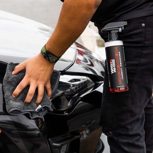 Person cleaning a car with a towel and holding a bottle of window cleaner.