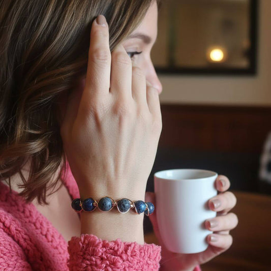 Woman holding a white mug with a blue beaded bracelet on her wrist, in a cozy indoor setting.