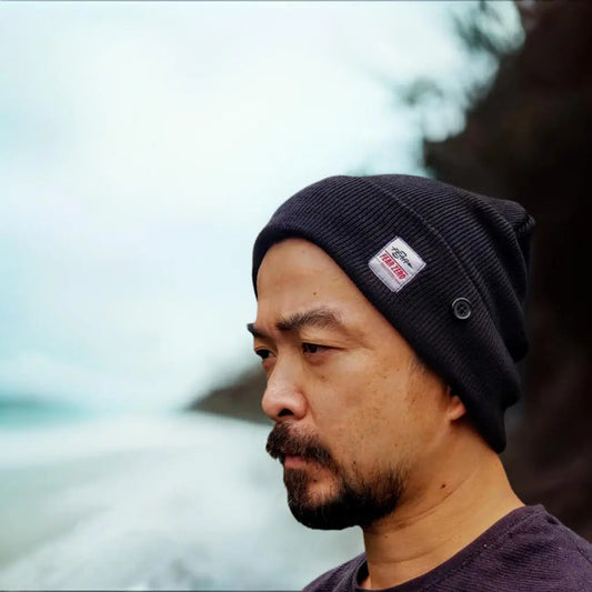 Man wearing a black beanie with a logo, looking to the side with a blurred natural background