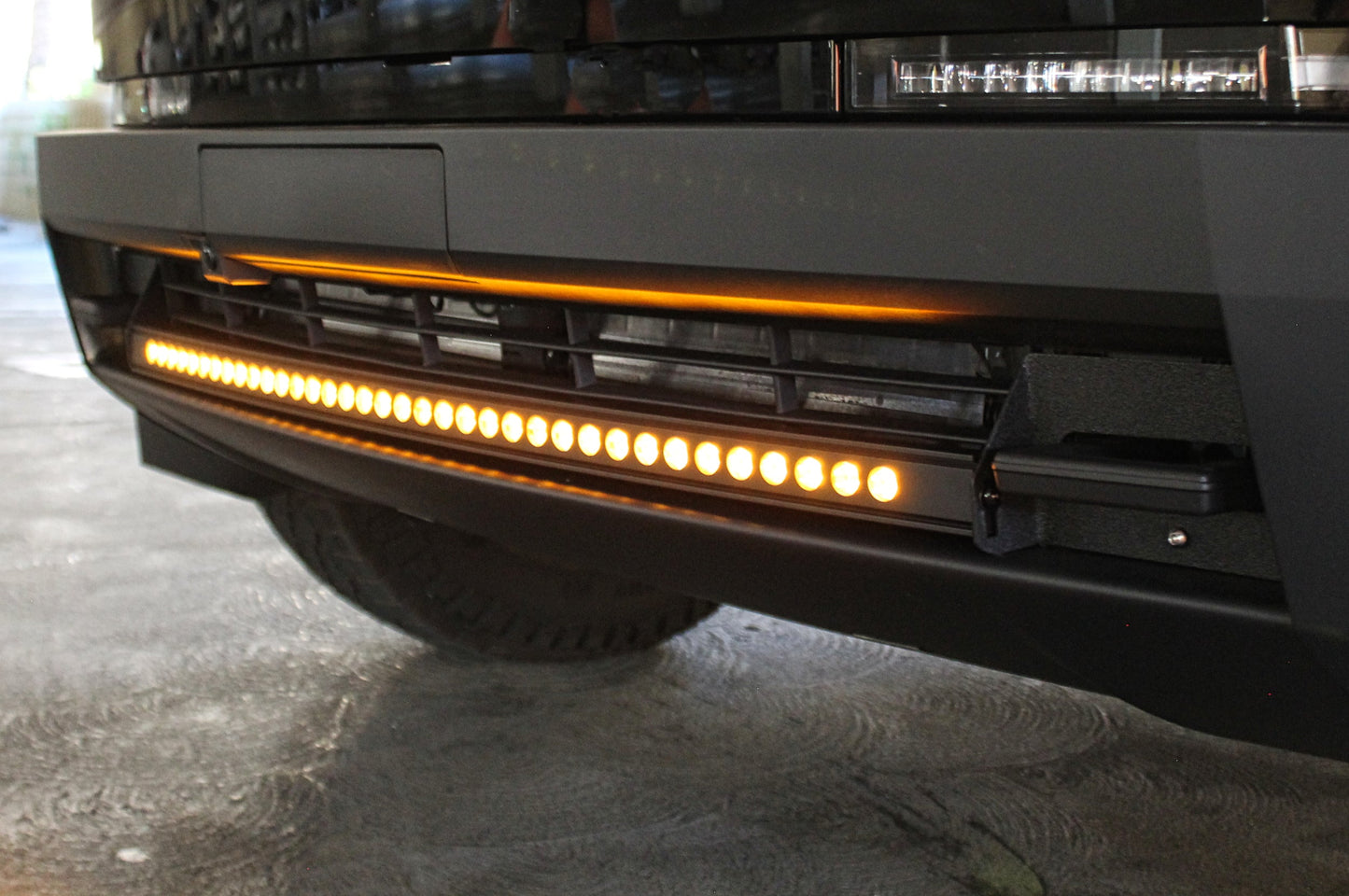 Close-up of a vehicle's front bumper with an LED light bar on a concrete surface.