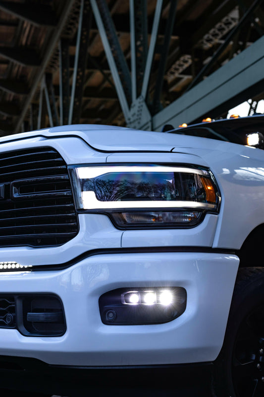 Close-up of a white truck's front headlight and grille in an indoor setting.