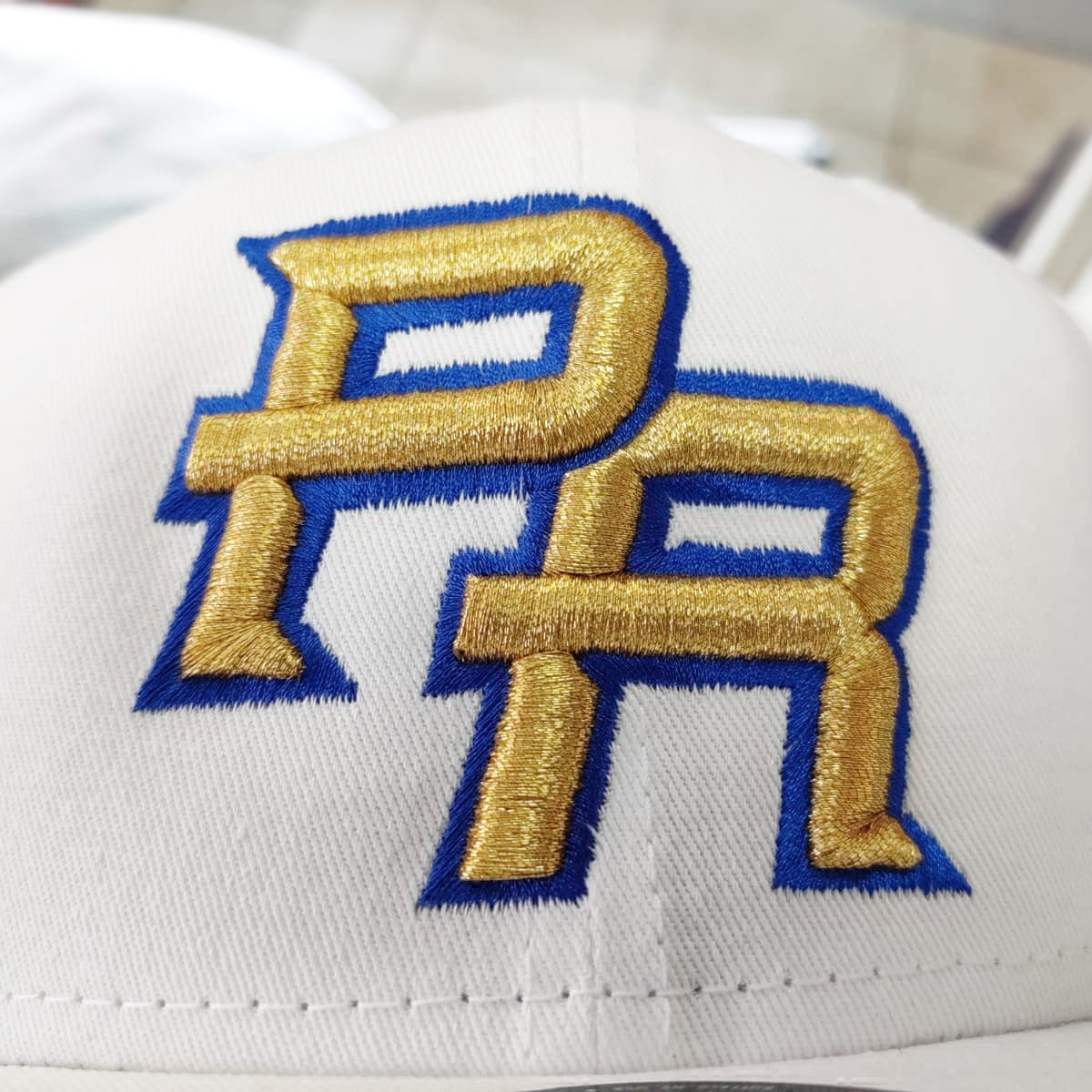 White cap with gold and blue embroidered PR - Puerto Rico logo on a blurred background