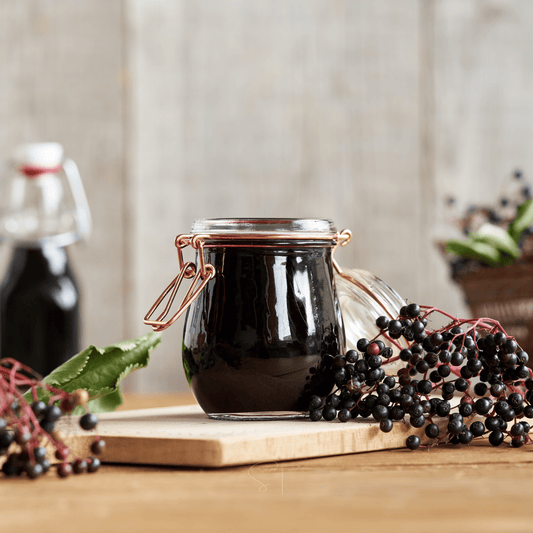 Jar of dark liquid on a wooden surface with elderberries around
