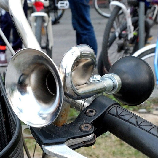 Bicycle horn attached to a handlebar with a blurred background of bicycles.