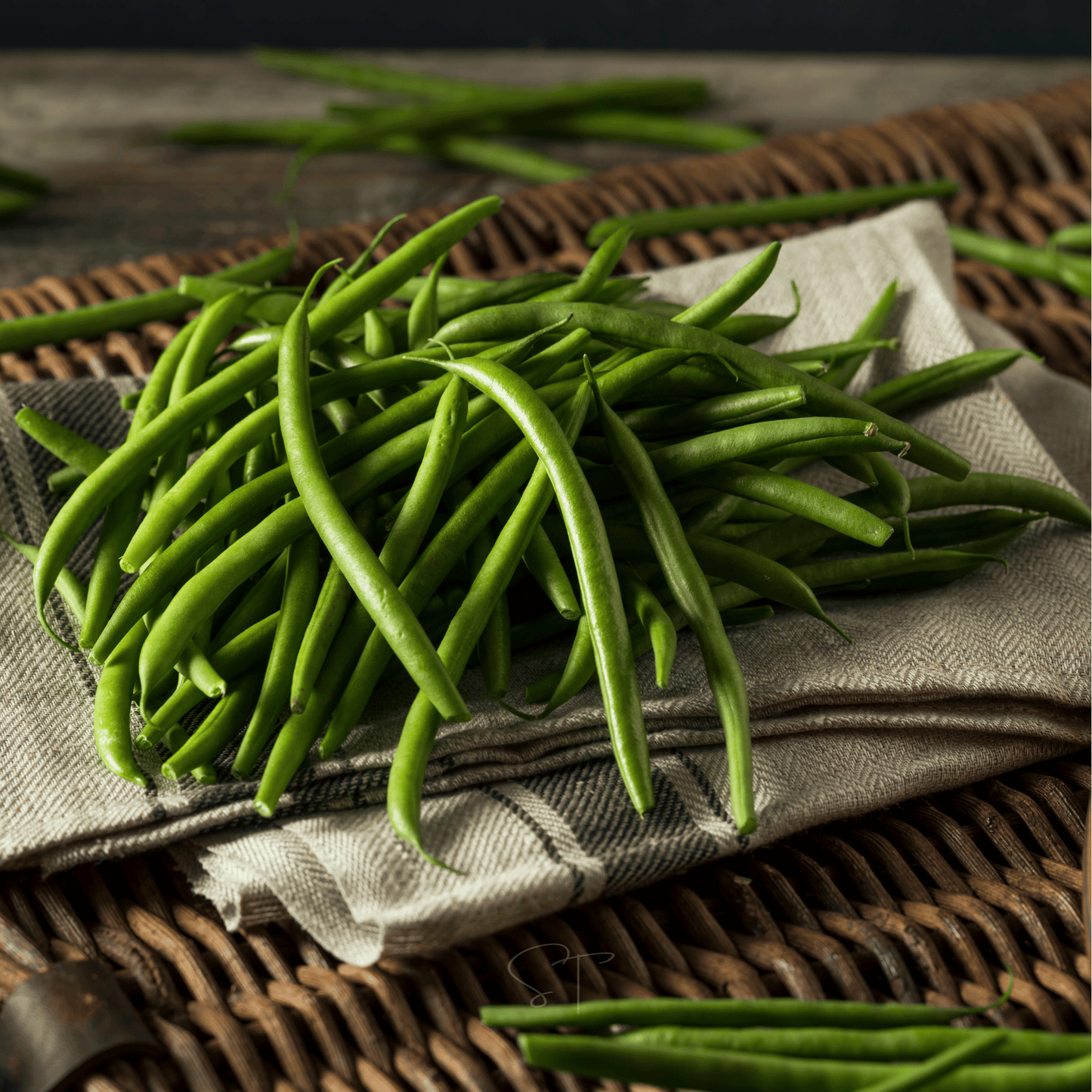 Green beans on a textured fabric surface with a woven basket in the background