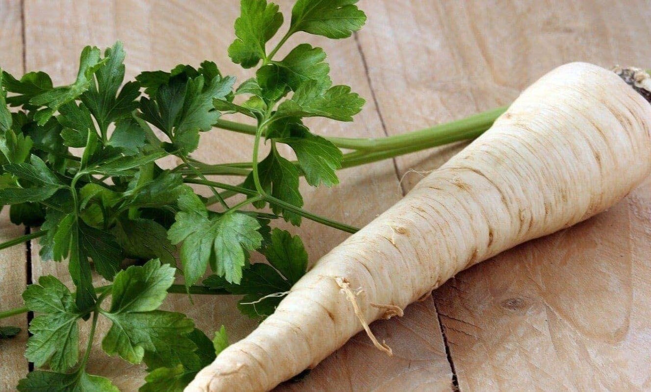 White parsnip with green leaves on a wooden surface