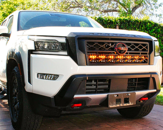 Front view of a white Nissan truck with illuminated grille in an outdoor setting