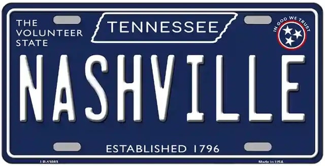 A metal license plate style sign with a blue background and white text that reads 'NASHVILLE ESTABLISHED 1796' with a small 'The Volunteer State' emblem at the top left corner and a 'TENNESSEE' abbreviation at the top center.
