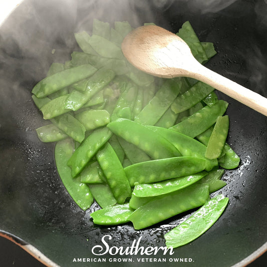 Green vegetables being cooked in a wok with a wooden spoon, featuring the 'Southern' brand logo.