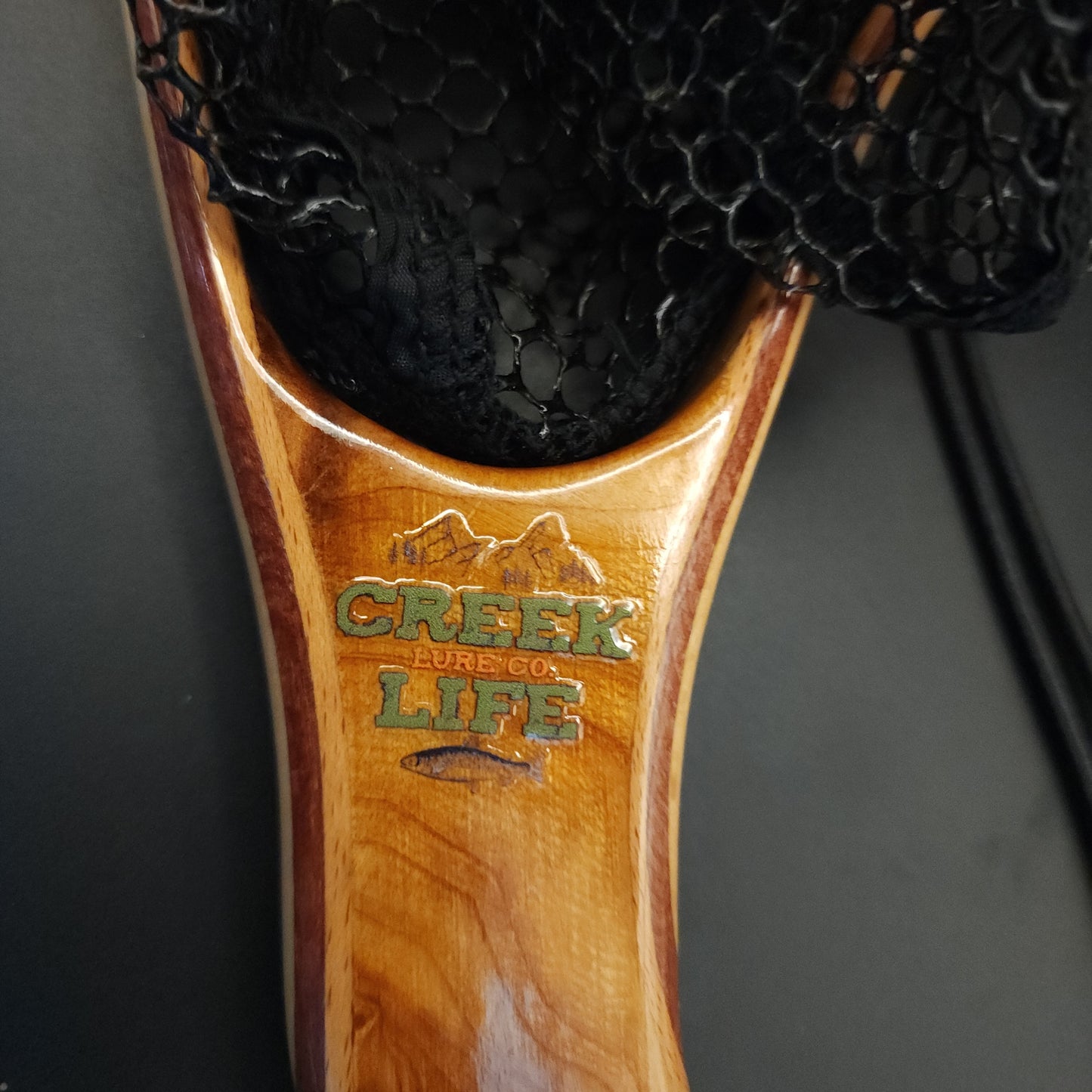 Wooden handle fishing net and 'Creek Life' branding on a dark background