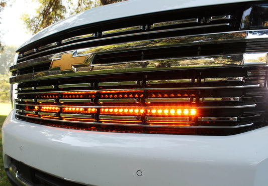 Close-up of a white truck's front grille with visible Chevrolet logo and Amber LED lights.