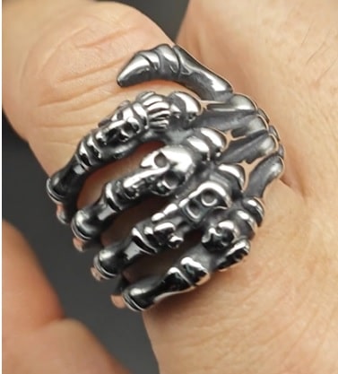 Silver skeleton hand ring on a finger against a neutral background