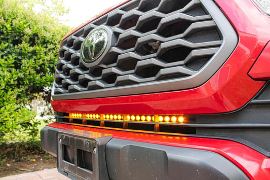 Close-up of a red vehicle's grille with a prominent amber light bar, set against a natural background.