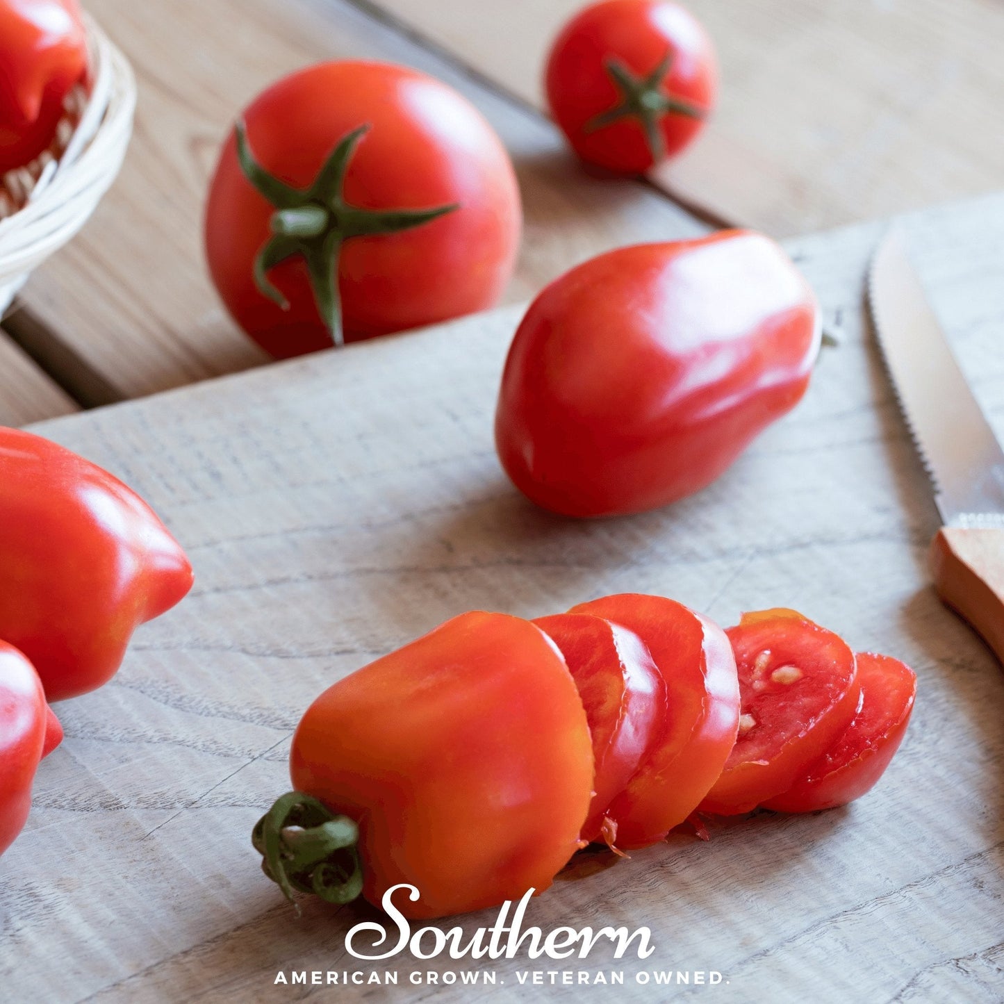 Sliced sauce tomatoes on a wooden cutting board with a knife, surrounded by whole tomatoes.