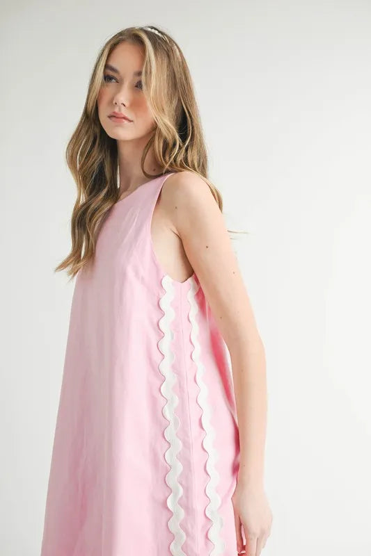 Woman wearing a pink dress with white scalloped edges on a white background