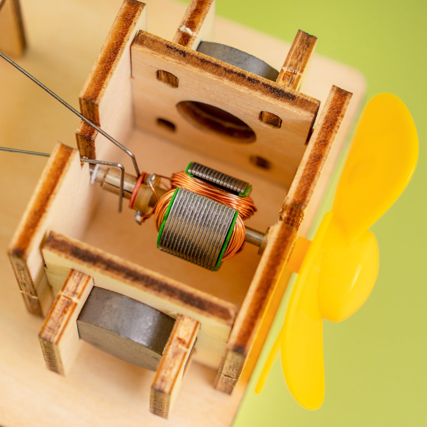 Close-up of a wooden mechanical model with a yellow propeller on a green background