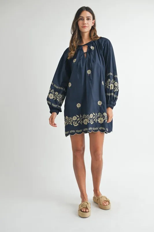 Woman wearing a navy blue dress with floral embroidery on a white background