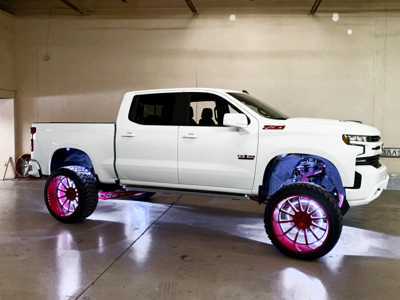 White pickup truck with large custom wheels and underbody lighting in a garage