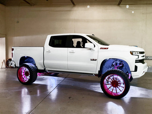 White pickup truck with large custom wheels and underbody lighting in a garage