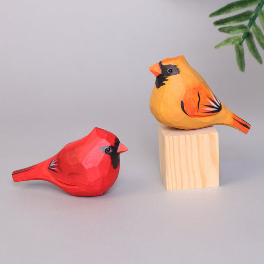 Two wooden cardinal bird figurines, one red and one orange, on a gray background.