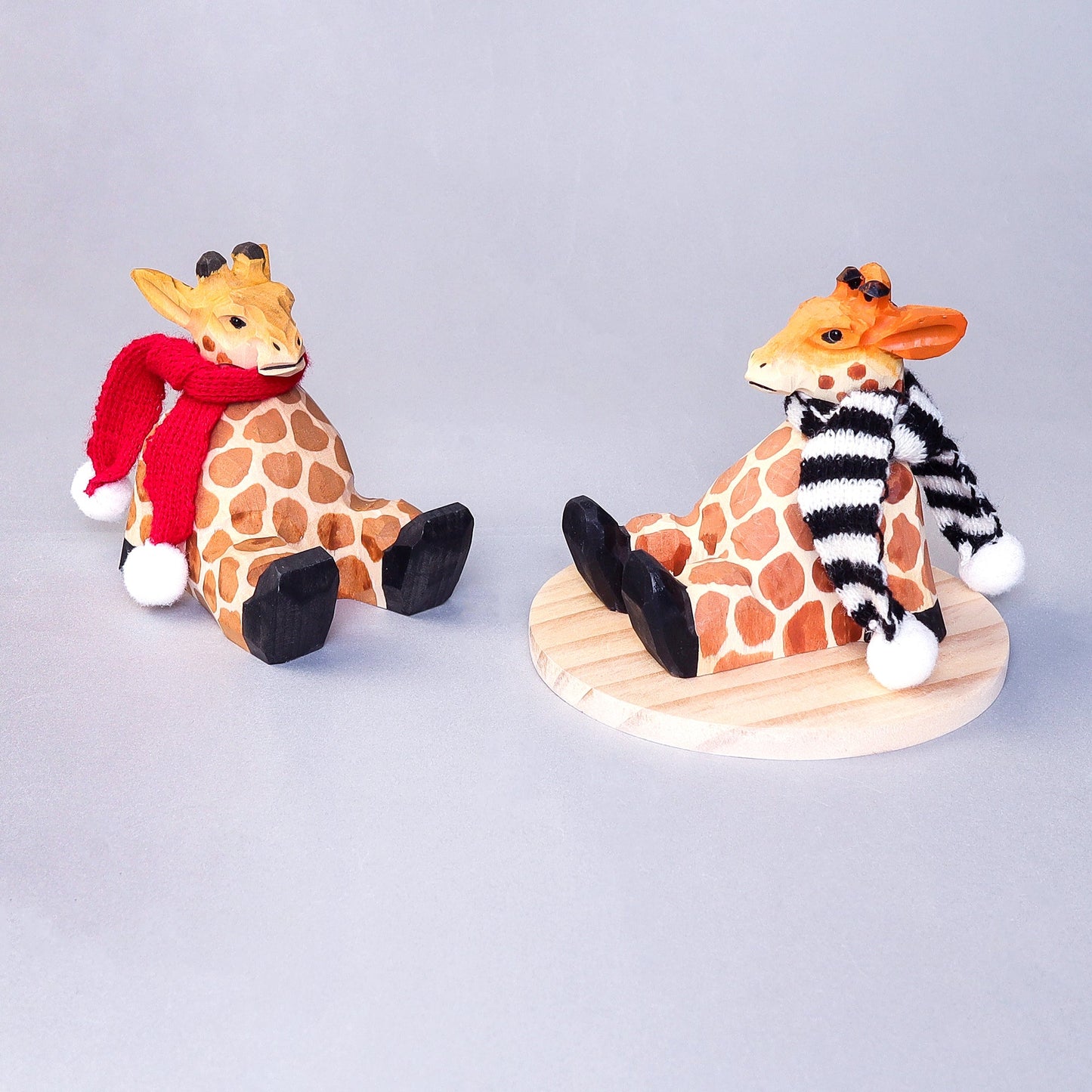 Two giraffe figurines wearing scarves on a gray background