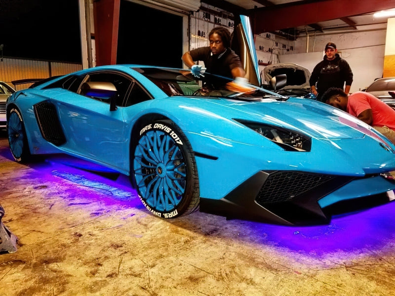 Blue sports car in a garage with people around and underbody lighting