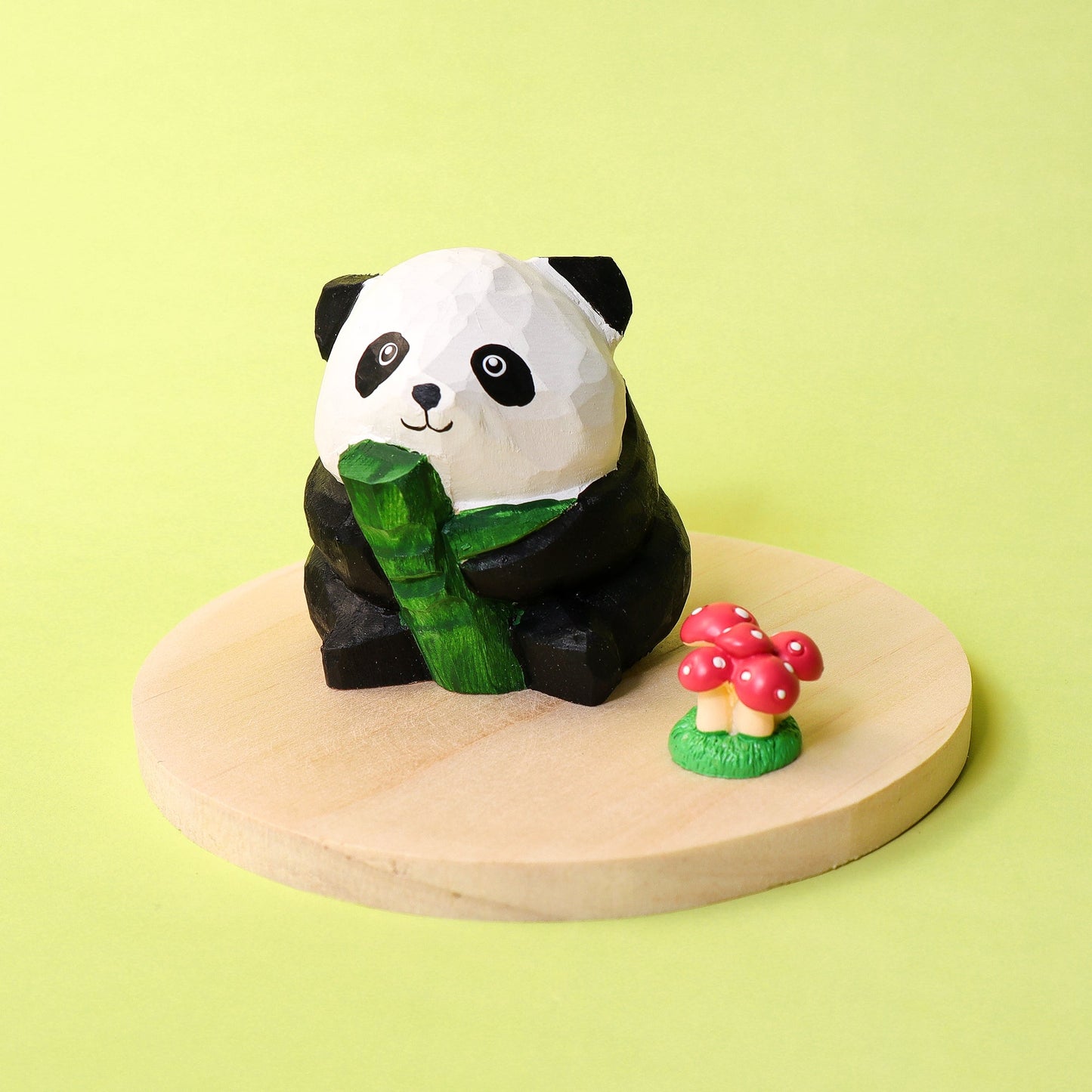 Panda figurine holding bamboo on a wooden platform with a small mushroom decoration against a light green background