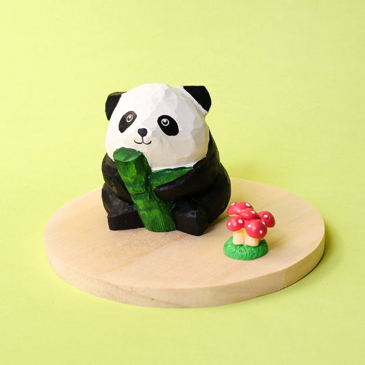 Panda figurine holding bamboo on a wooden platform with a small mushroom decoration against a light green background