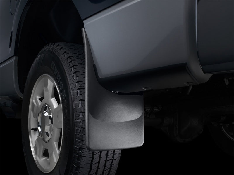 Car mud flap attached to a vehicle tire on a dark background