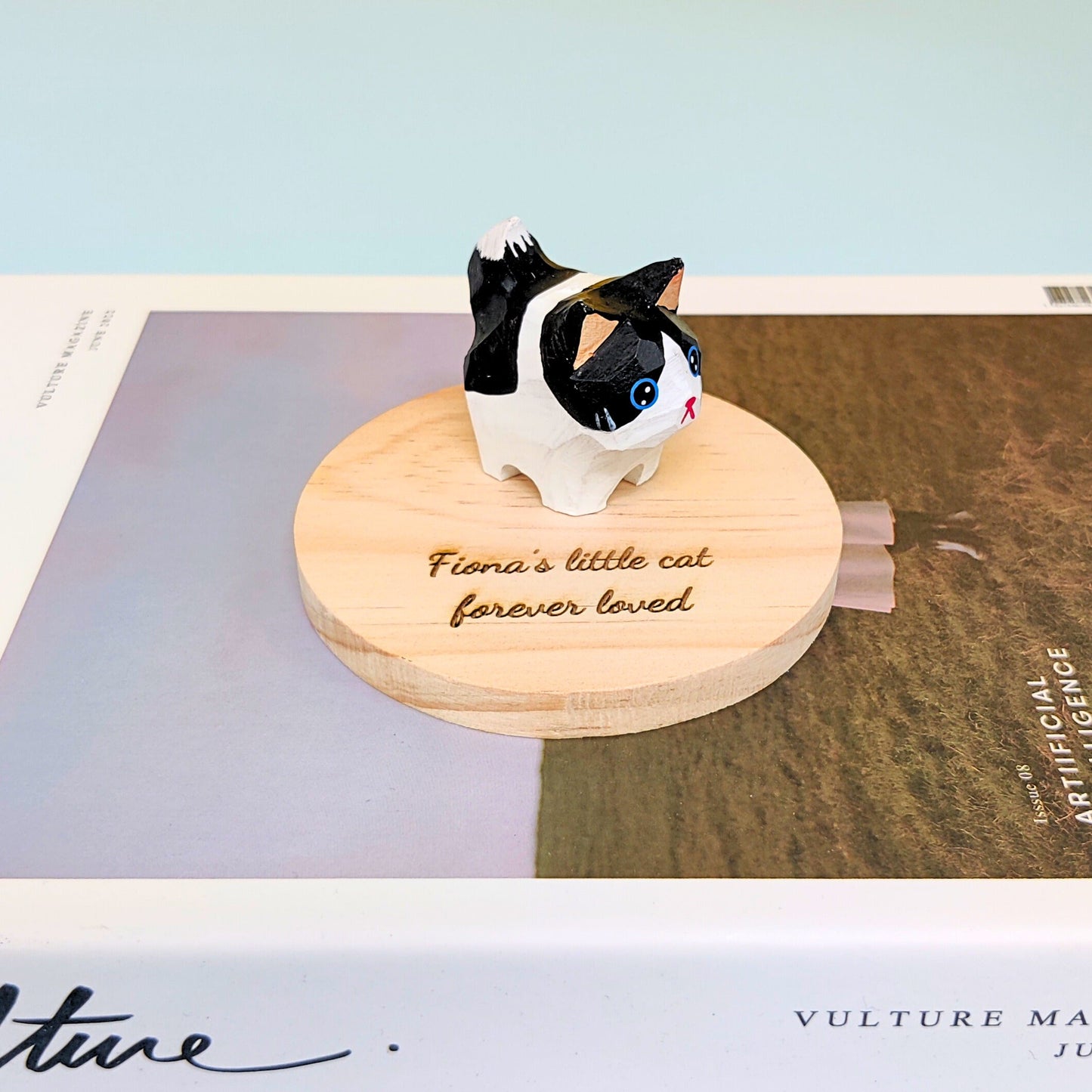 Cat figurine on a wooden base with engraved text, placed on a magazine.