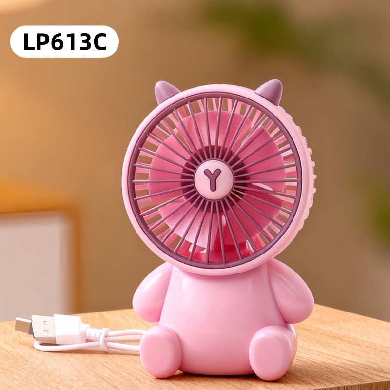 Pink cartoon-style fan on a wooden surface with a blurred background