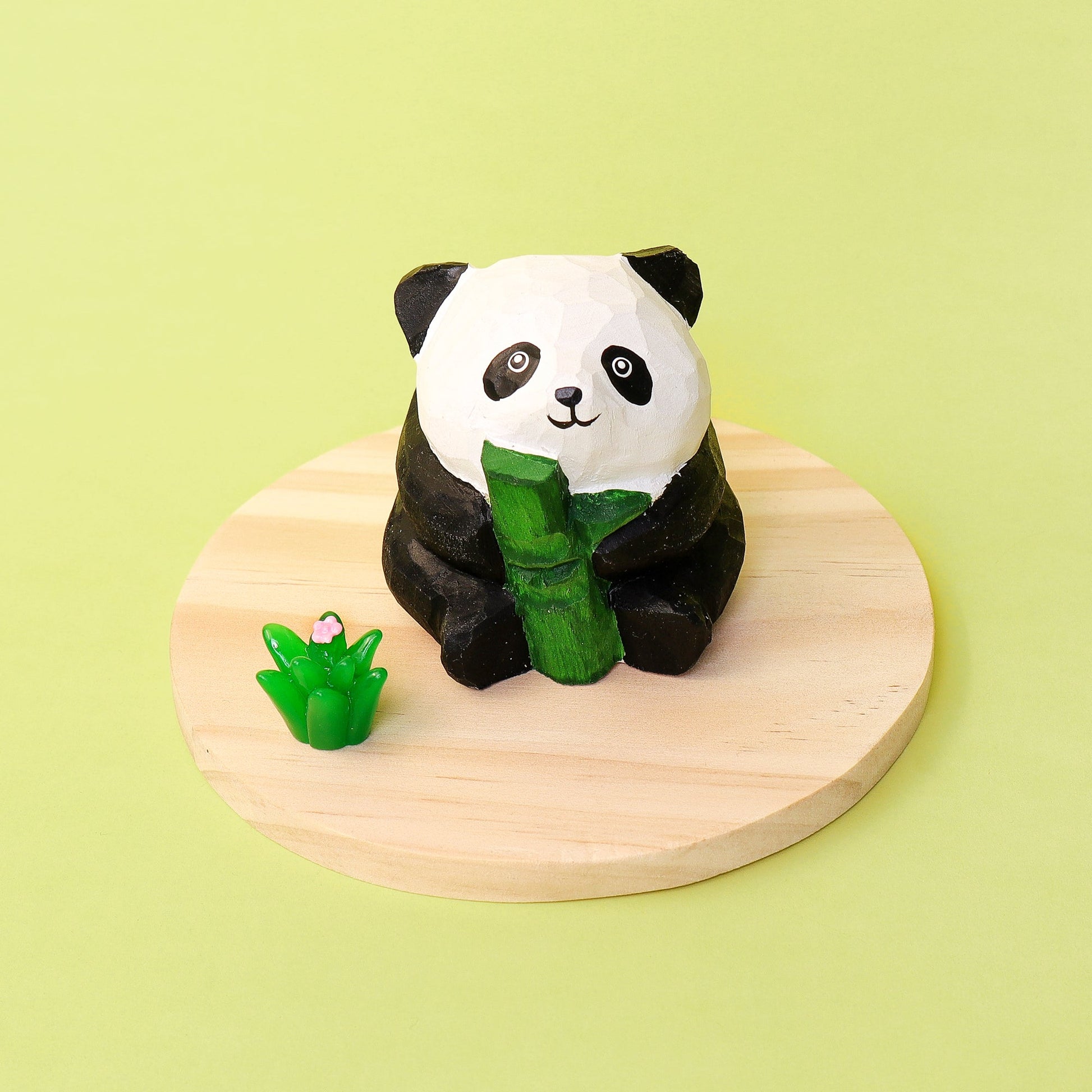 Panda figurine holding bamboo on a wooden platform with a green background