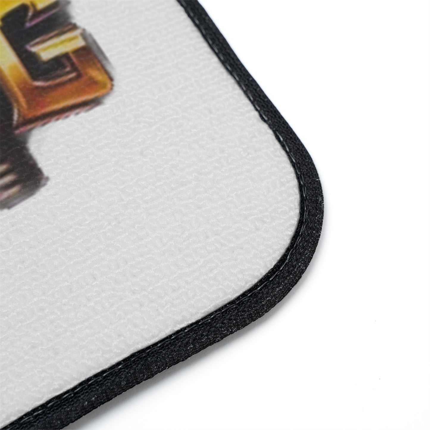 Close-up of a white textured floor mat with a black stitched border and part of a gold and black graphic design visible on a white background.
