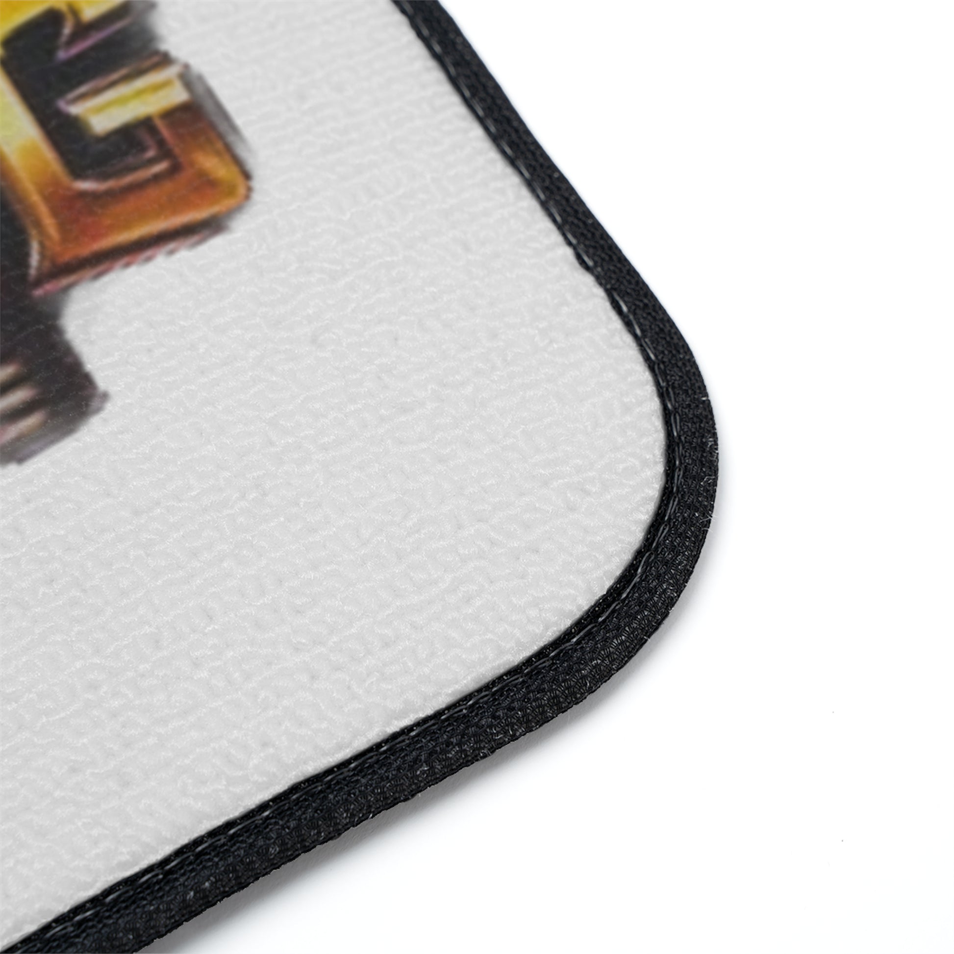 Close-up of a white textured floor mat with a black stitched border and part of a gold and black graphic design visible on a white background.
