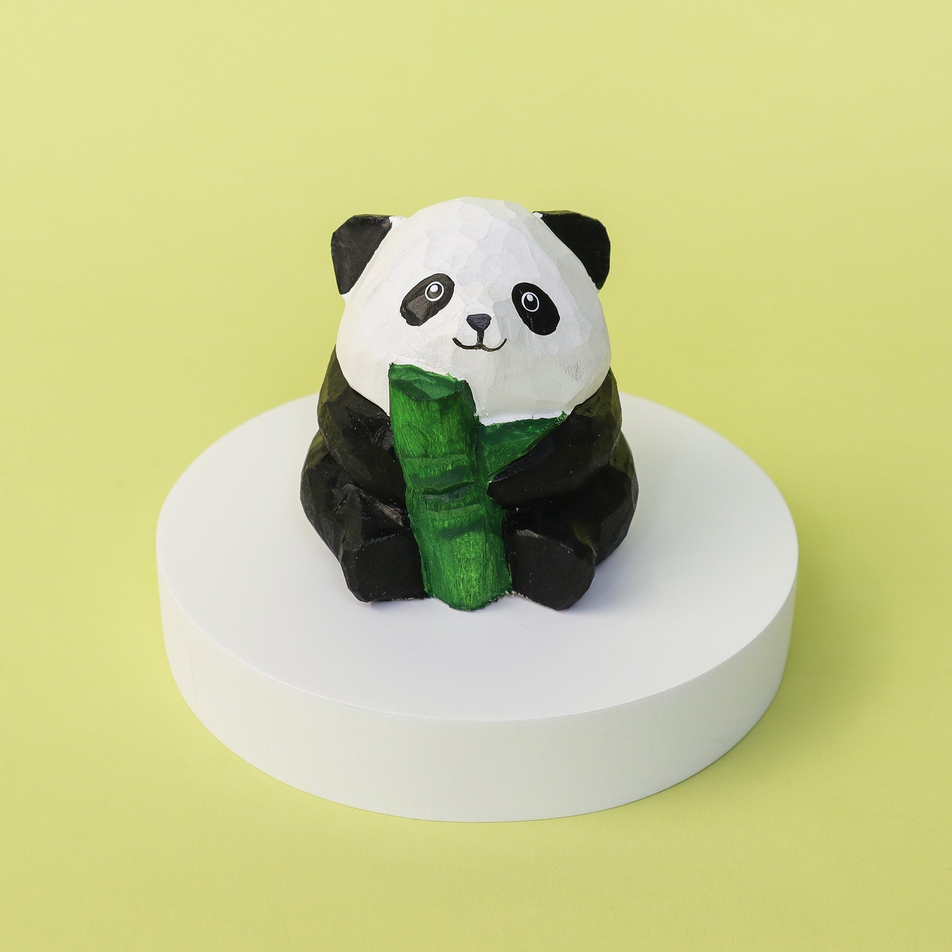 Panda figurine holding bamboo on a white platform with a yellow background